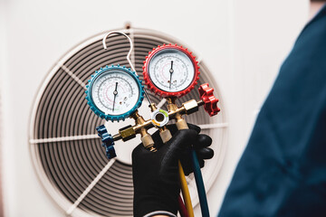Technician holding manifold gauge measuring tool on fan for check pump filling home air conditioner...