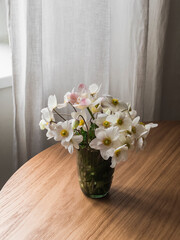 A bouquet of anemones in a glass cup on a round wooden table