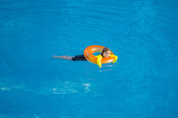 Kid playing with inflatable ring in swimming pool on hot summer day. Kid with inflatable ring in swimming pool. Summer vacation. Summer holiday. Summertime kids weekend.