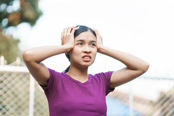 A young Asian woman appears panicked outside her home. She exhibits signs of anxiety, fear, and distress. Her expression reflects feelings of stress and unease.