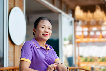 Asian middle-aged woman sitting in front of glass door of her house.