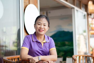 Asian middle-aged woman sitting in front of glass door of her house.