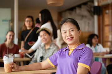 Asian mid adult woman sits in the middle of the cafe, soft focus, blurred people in cafe background.