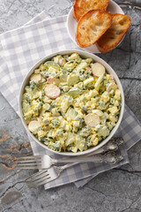 Homemade salad of eggs, radishes, green onions and cucumber dressed with mayonnaise close-up in a bowl on the table. Vertical top view from above