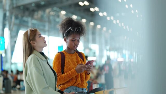 Woman friends looking flight schedule on timetable and go to check-in and boarding gate together in airport terminal. Attractive girl traveler travel by airplane transportation on holiday vacation.