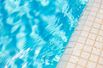 Natural sunlight blur bokeh white marbles closeup of swimming pool edge and clear blue water. New...