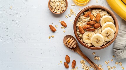 Ingredients for preparing oatmeal in a wooden bowl with almonds banana slices honey oat flakes and a spoon on a white surface Top view with space for text - Powered by Adobe