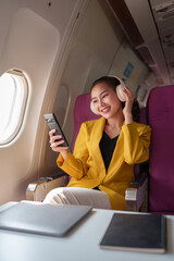 A business woman in a yellow suit with headphones around her neck has fun using a smartphone to listen to music. Make an online video call on an airplane with a Wi-Fi connection. Business travel.