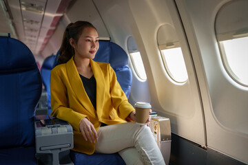 Confident businesswoman in formal clothes looking out of airplane window during flight while...