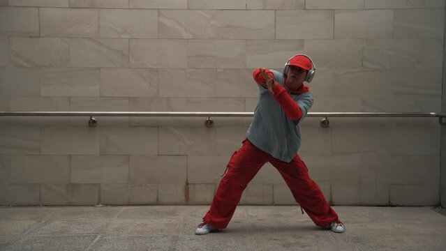 Handsome choreographer practice street dance in gray background. Young attractive b boy dancer perform while wearing stylish cloth. Feeling of lively step. Copy space. Outdoor sport 2024. Sprightly.
