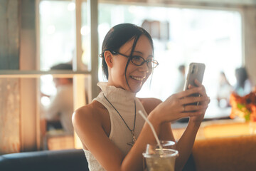 Asian woman gen z in Y2K trendy fashion styles Using smartphone for online dating app at indoor cafe