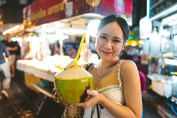 Asian tourist woman eating coconut juicetraveling at China town asia street food night market