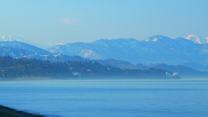Sea Horizon And Peaks Of Mountains In Distance In Haze. Haze Under Clear Blue Sky. Still.