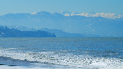 Snow Mountains In Haze Across The Bay At A Great Distance. Sunrise At Beach With Snowy Mountains....
