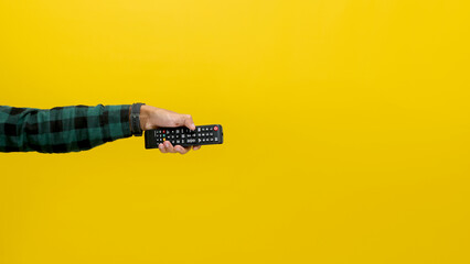Hand Holding a Black TV Remote, Isolated on a Yellow Background