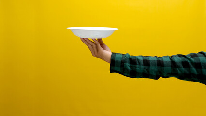 Hand holding empty white plate isolated on a yellow background