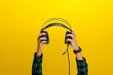 Hand grips a black headphone against a bright yellow background. Ideal for illustrating concepts...