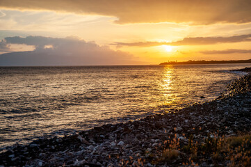 Hawaiian sunset casts a warm glow on the ocean and pebble shore