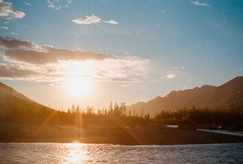 The sun peaks through the sky overlooking an Alaska River.