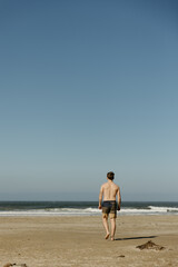 Shirtless man walking on beach towards ocean waves