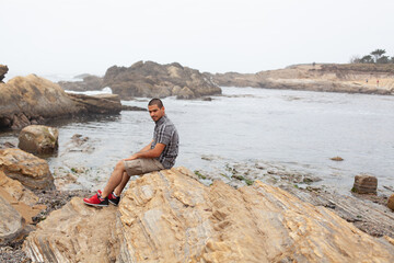 man sitting on rocks with body of water behind him