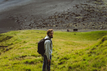 Man traveler hikes by the green hills in Iceland.