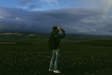 Man traveler with a backpack in Iceland takes photos with his phone.