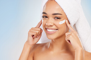 Portrait, cream and woman with towel in studio for skincare routine, benefits and dermatology. Female person, point and lotion with smile for collagen glow, shine and cosmetics on blue background