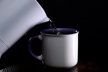 Duży porcelanowy kubek zalewany gorąca wodą na herbatę na czarnym tle 
