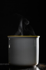 Ceramiczny kubek na kawę na czarnym tle z podświetlona od tyłu parą wodną unosząca się nad...