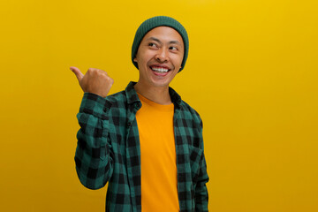An excited young Asian man, dressed in casual clothes and wearing a beanie hat, is pointing with...