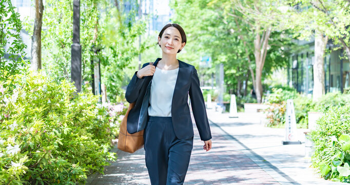 新緑の中を歩くスーツを着た女性