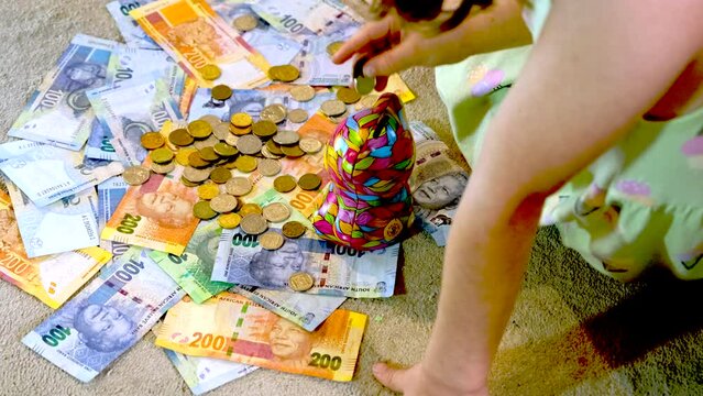 Girl takes coins on top of South African banknotes and deposits into money box