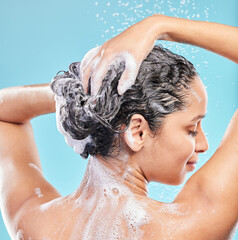 Naklejka premium Back, shower and woman with skincare, wellness and hair care on blue studio background. Rear view, person and model with water drops, wet or beauty with liquid, grooming routine and foam with hygiene