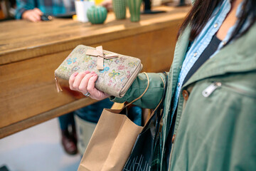 Close up of unrecognizable woman client holding wallet with bow and ecological shopping paper bags...