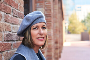 Smiling woman in beret by brick wall, casual style
