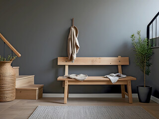 Wooden bench with a hanging cloth piece against a grey wall and wooden staircase. Scandinavian, rustic farmhouse interior design. Indoor plant pots in beige color floor and floor rug.