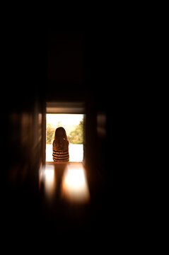 Young child sitting in bight door frame of dark room