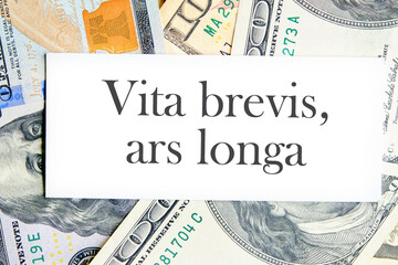 Ars longa, vita brevis ancient Latin saying meaning - Art is long, life is short, on a white business card lying on dollars