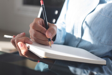 Woman hand with a pencil writing on paper notebook. Female student taking note on lecture chair during studying in classroom. business planning, to do list reminder