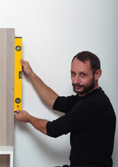 Man with a cheerful expression using a yellow level tool to ensure vertical alignment a piece of...