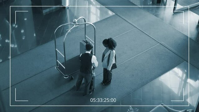 High angle surveillance footage of elegant Black female traveller arriving at hotel, passing suitcase to young Asian porter in uniform, who is putting it on cart and showing woman to reception