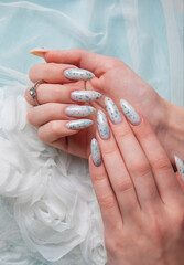 Female hands with blue nail design on blue silk background.