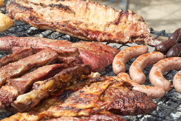 Close up view of pieces of beef and sausage cooking on the grate of a barbecue for a friends outing. Summer barbecue.