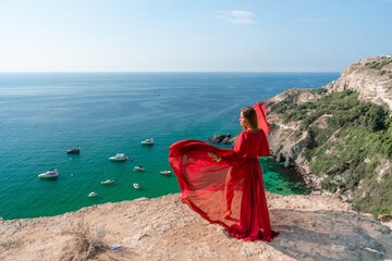 Red Dress Woman sea Cliff. A beautiful woman in a red dress and white swimsuit poses on a cliff overlooking the sea on a sunny day. Boats and yachts dot the background.