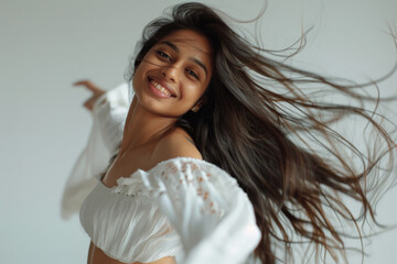 A young happy Indian ethnic female with flowing hair dancing against a white background