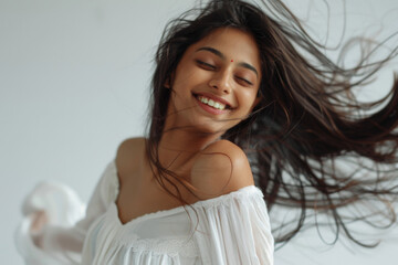 A young happy Indian ethnic female with flowing hair dancing against a white background
