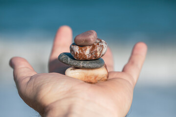 Open hand with a stack of four pebbles of different colors on a beach in flat daylight that convey...