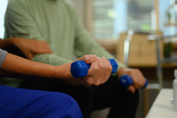Nurse or physiotherapist caregiver helping senior man exercising with dumbbell at home