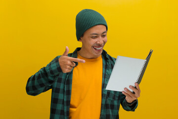 An excited young Asian student, dressed in a beanie hat and casual clothes, is pointing at a book...
